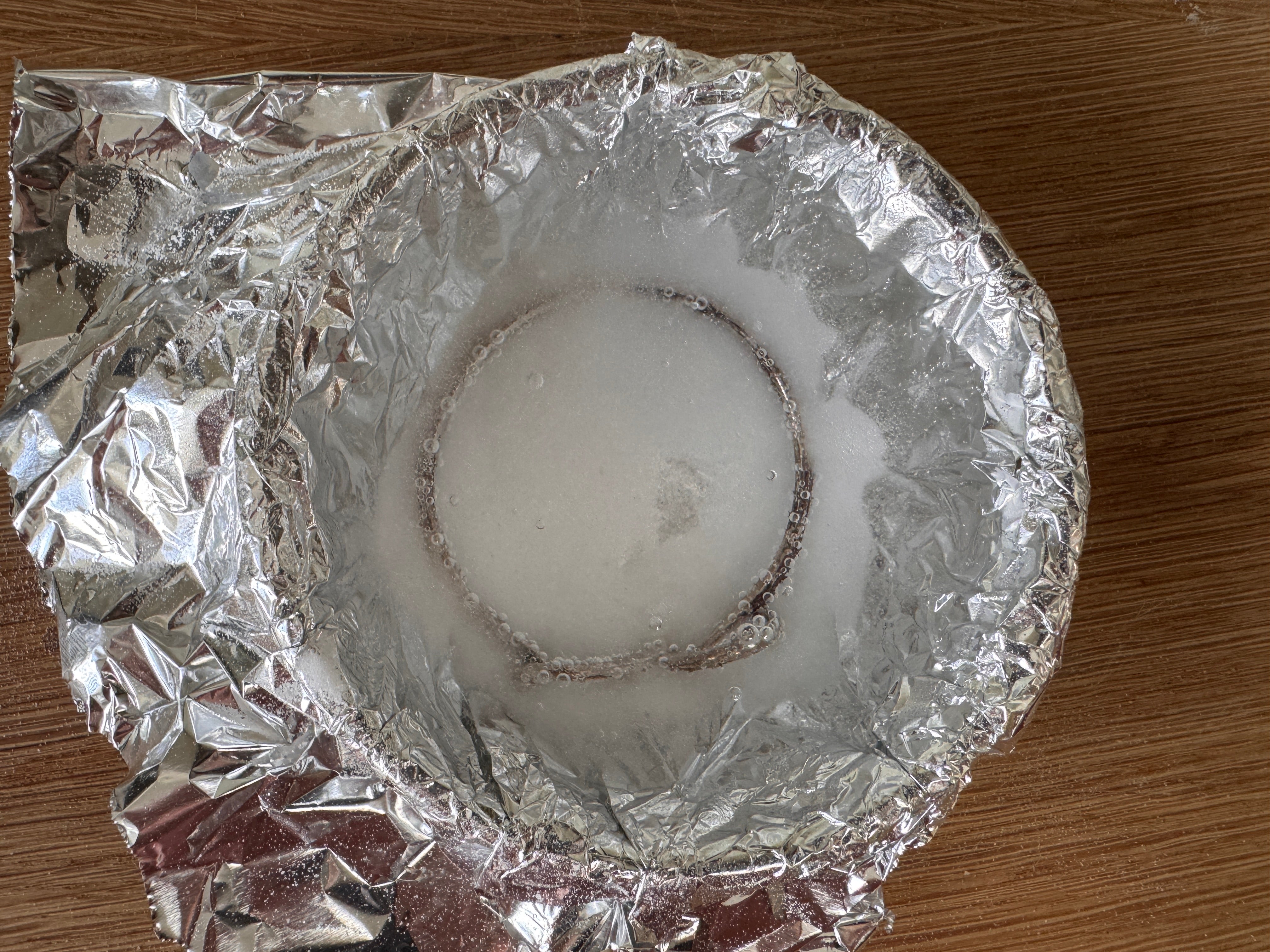 tin foil lined glass bowl with a silver bangle covered in baking soda and boiling water