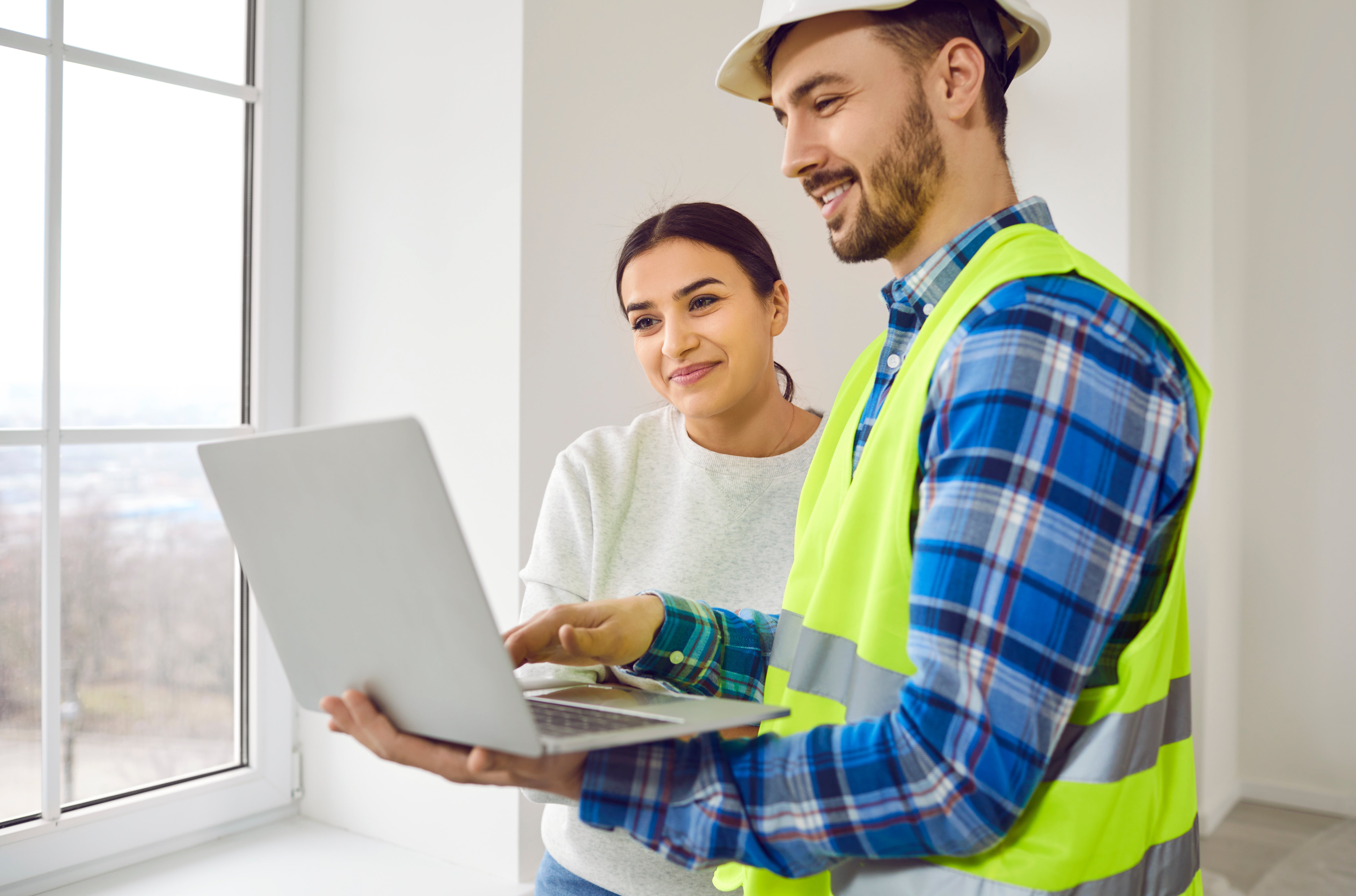 woman and tradesman looking at a laptop. He is wearing a hard hat and a high vis vest