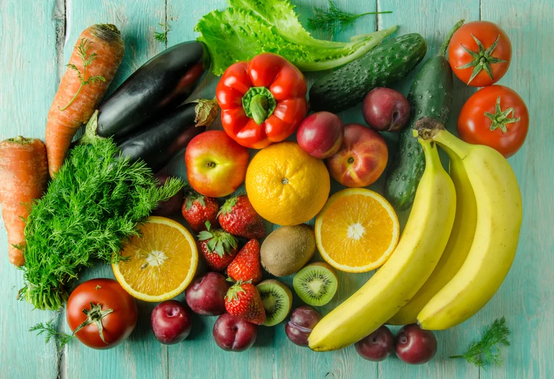 Fruit and vegetables lay on a wooden board. It includes carrots, zucchinis, lettuce, strawberries, bananas, oranges, plums, tomatoes and cucumber.