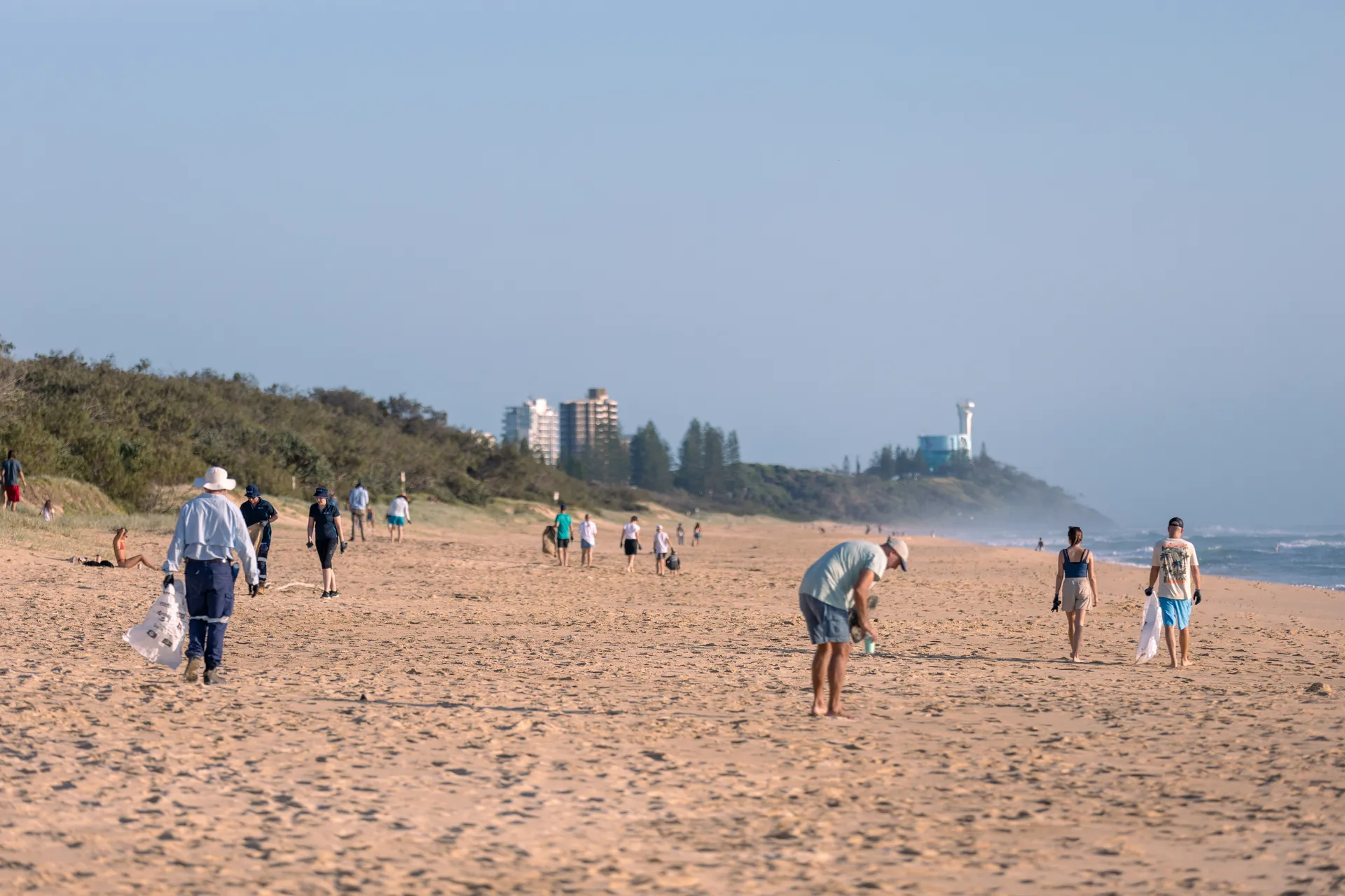 A group of people collecting rubbish on a sandy beach, working together to clean up the environment.