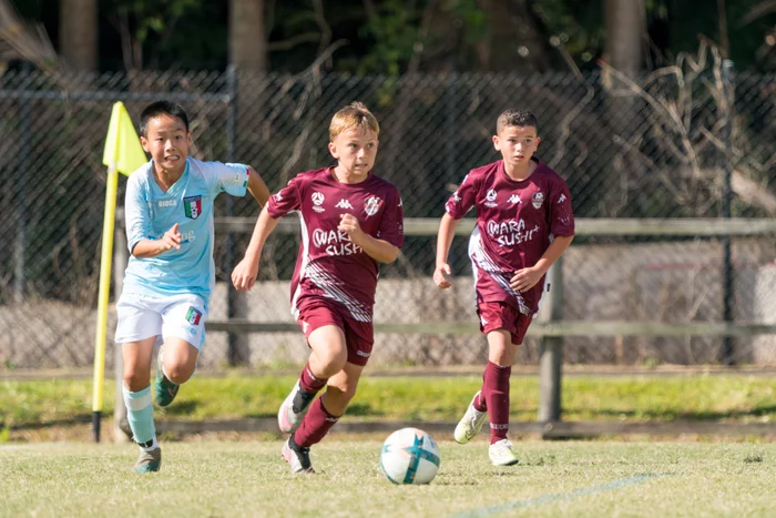 Three junior football players running towards the soccer ball.