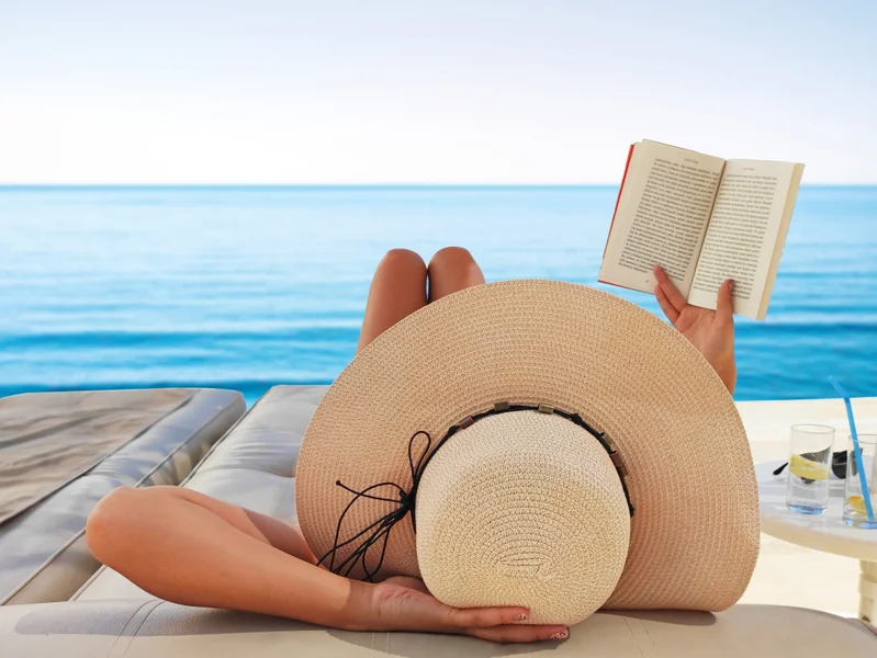 Lady by the beach reading one of the top adult reads this Summer