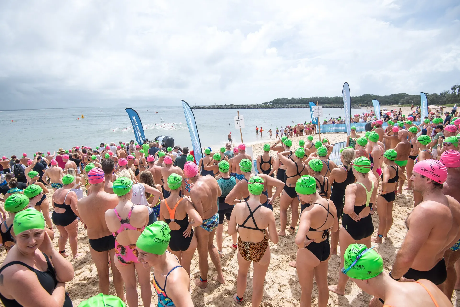 A mass of people waiting on the beach to complete in the Mooloolaba mile swim - wearing bright green and bright pink swim caps