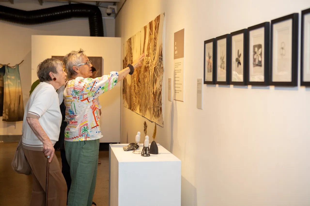 Two women discussing an artwork at the Wildflowering by Design exhibition launch