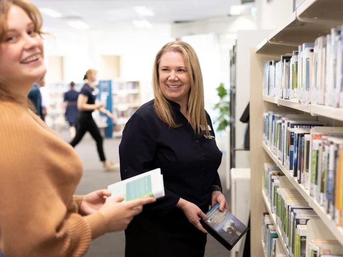 Staff at a library laugh together while holding books in front of a bookshelf.