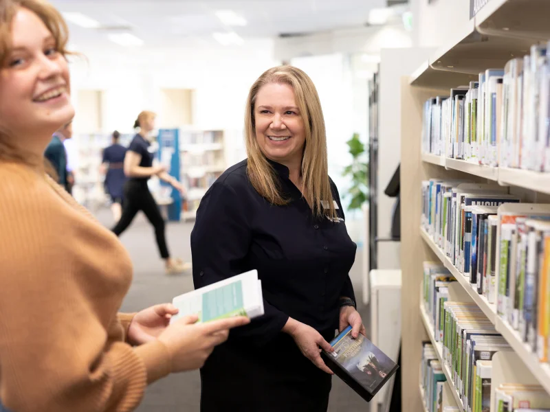 Staff at a library laugh together while holding books in front of a bookshelf.