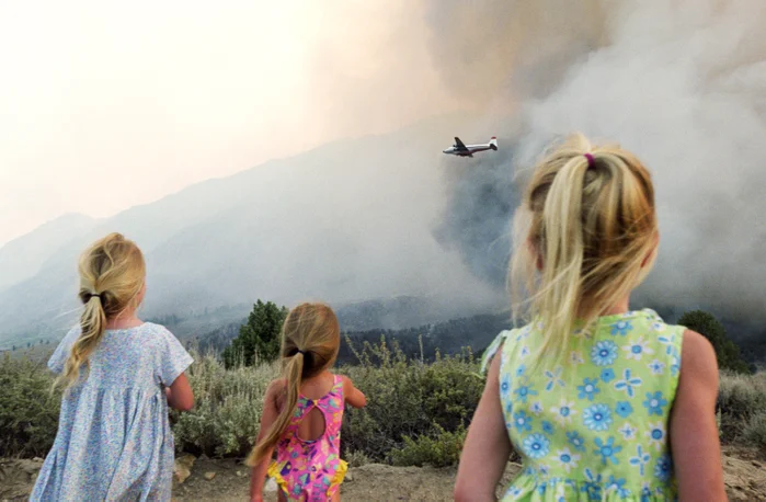 Three young girls watch as a plane drops water onto a bushfire.