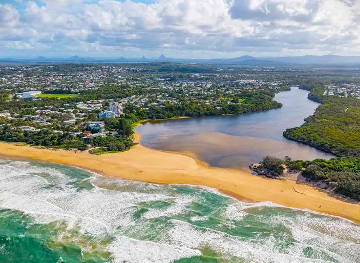 An aerial view of the Sunshine Coast shows a river and the ocean with a strip of sand between the two.