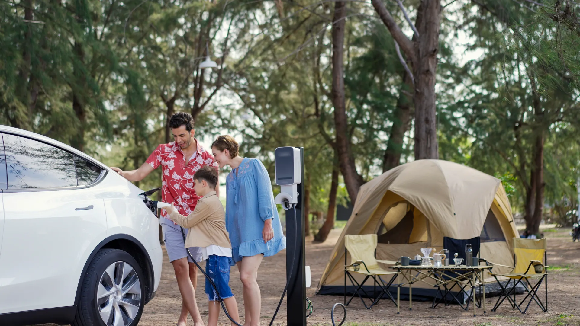 Couple and young son charge their EV with a tent in the background