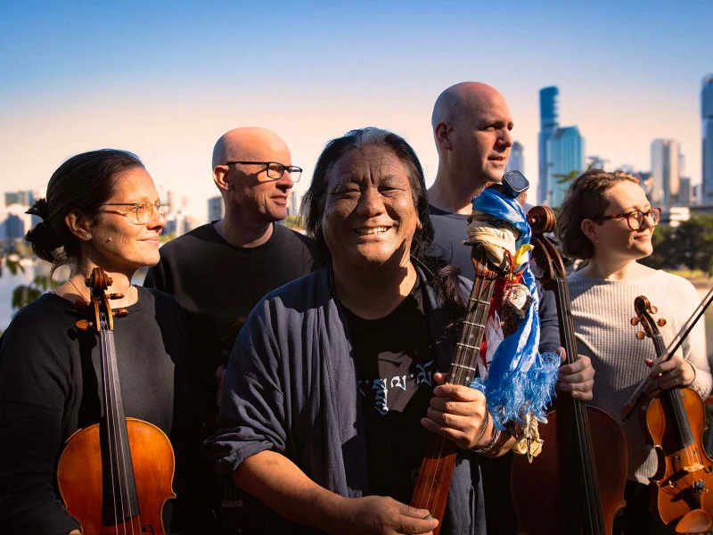 Whispering Sky musicians holding violins with City scape behind them.