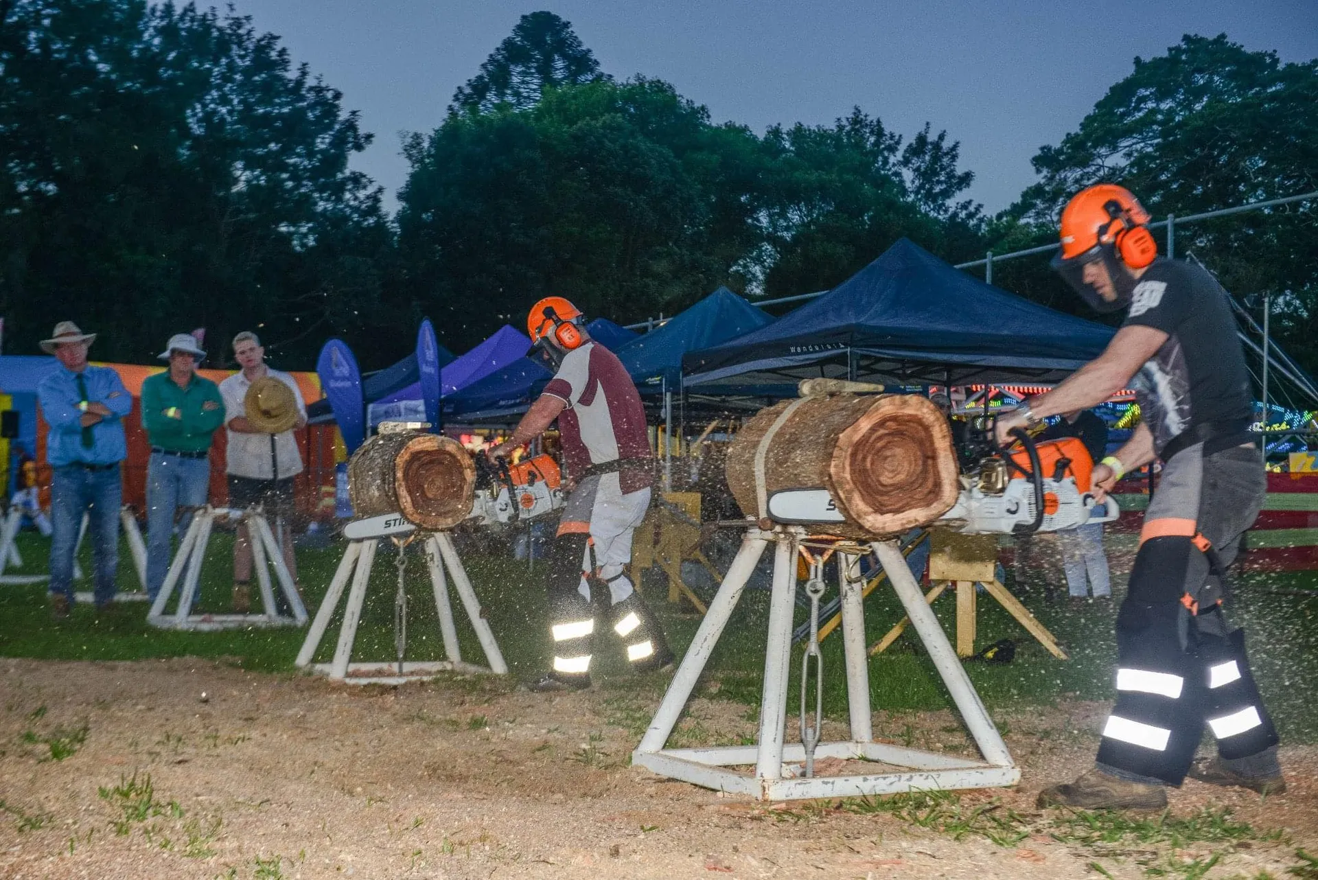 2 men in competition, with chainsaws chopping parts of a log on a special metal stand.