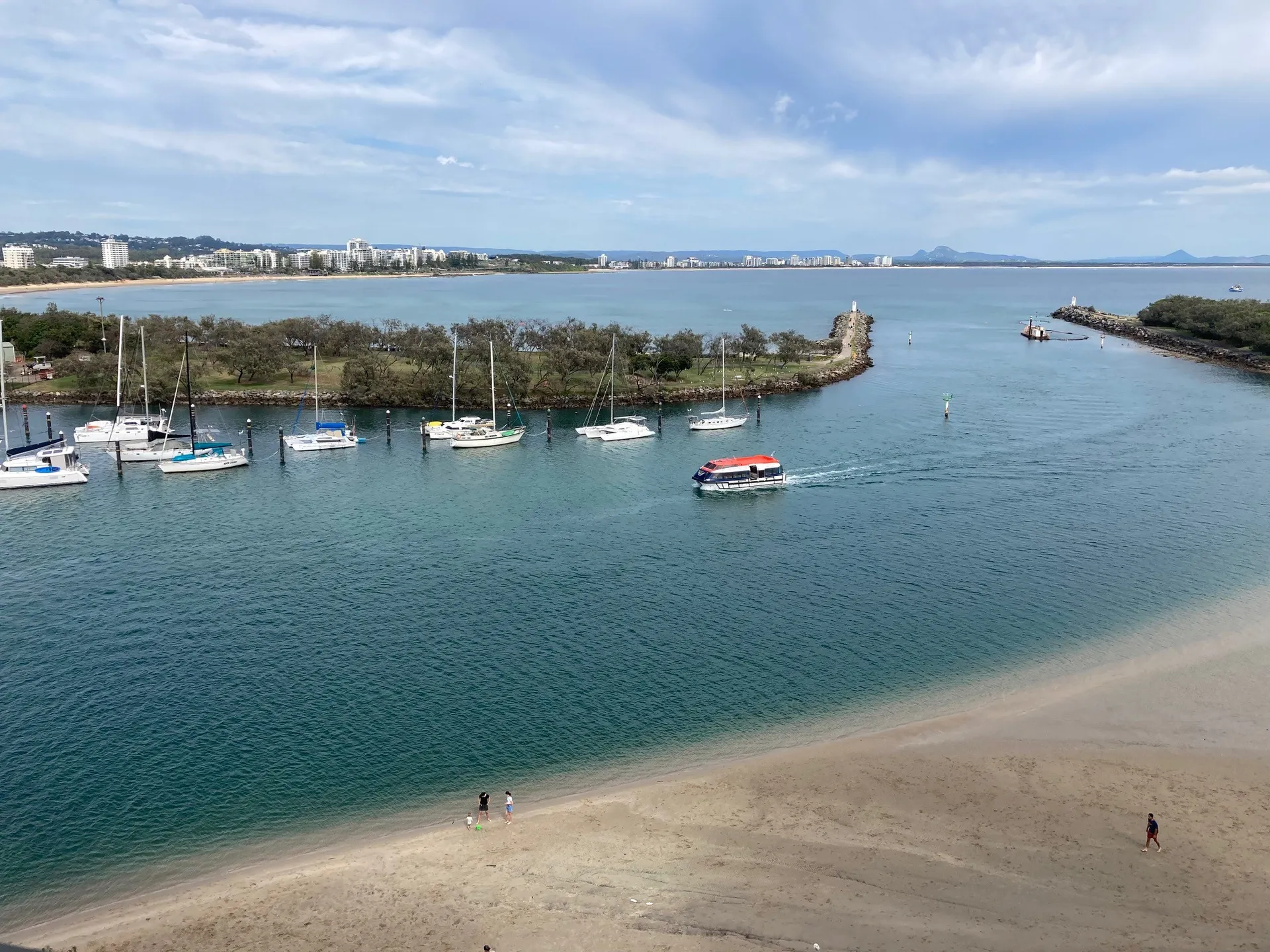 Boat coming into a calm waterway inlet with blue skies and fluffy white clouds. Above shot overlooking a sandy brown beach.