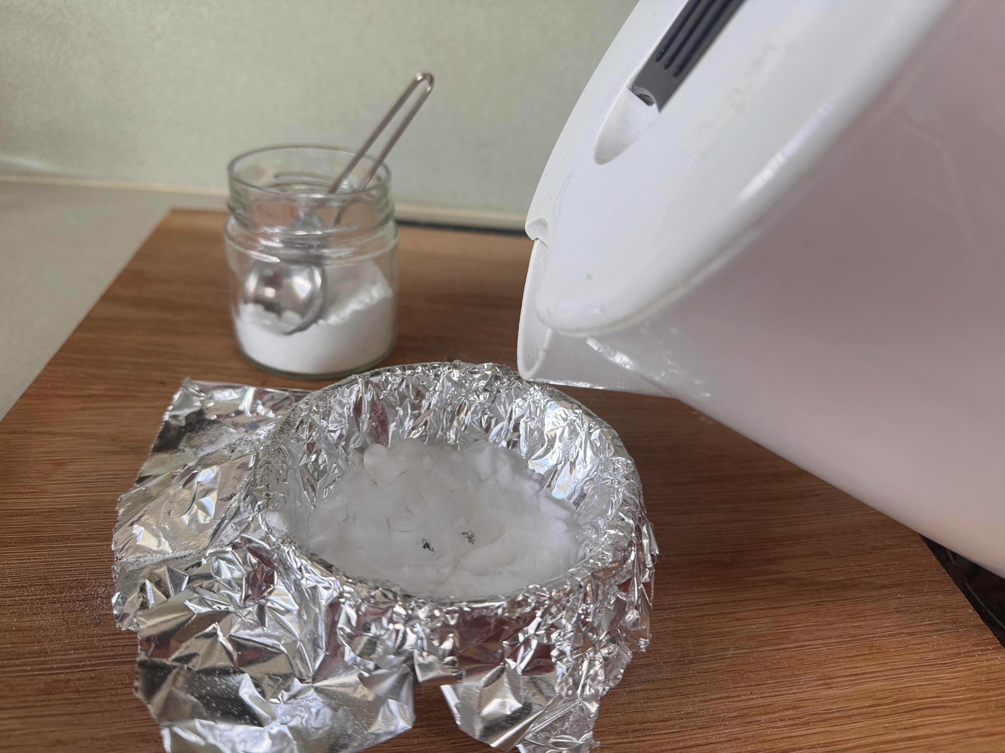 a kettle pouring water into a glass bowl lined with tin foil 