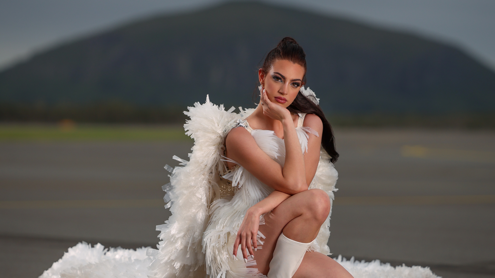 Model Jodi Urli wears Plastic Rain by Natalie Hamblin (2024 Runner-up Trashion). Jodi is poised on an airport runway, with a view of Mt Coolum behind her.