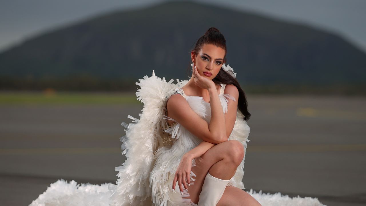 Model Jodi Urli wears Plastic Rain by Natalie Hamblin (2024 Runner-up Trashion). Jodi is poised on an airport runway, with a view of Mt Coolum behind her.