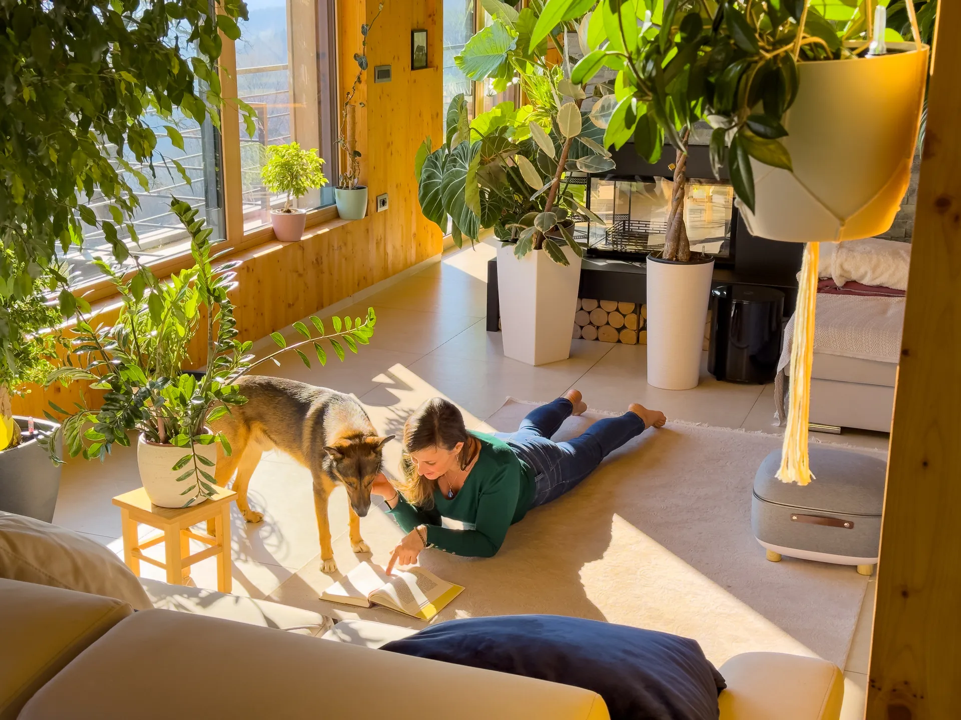 a woman and her dog laying on the ground in a house surrounded by thriving pot plants