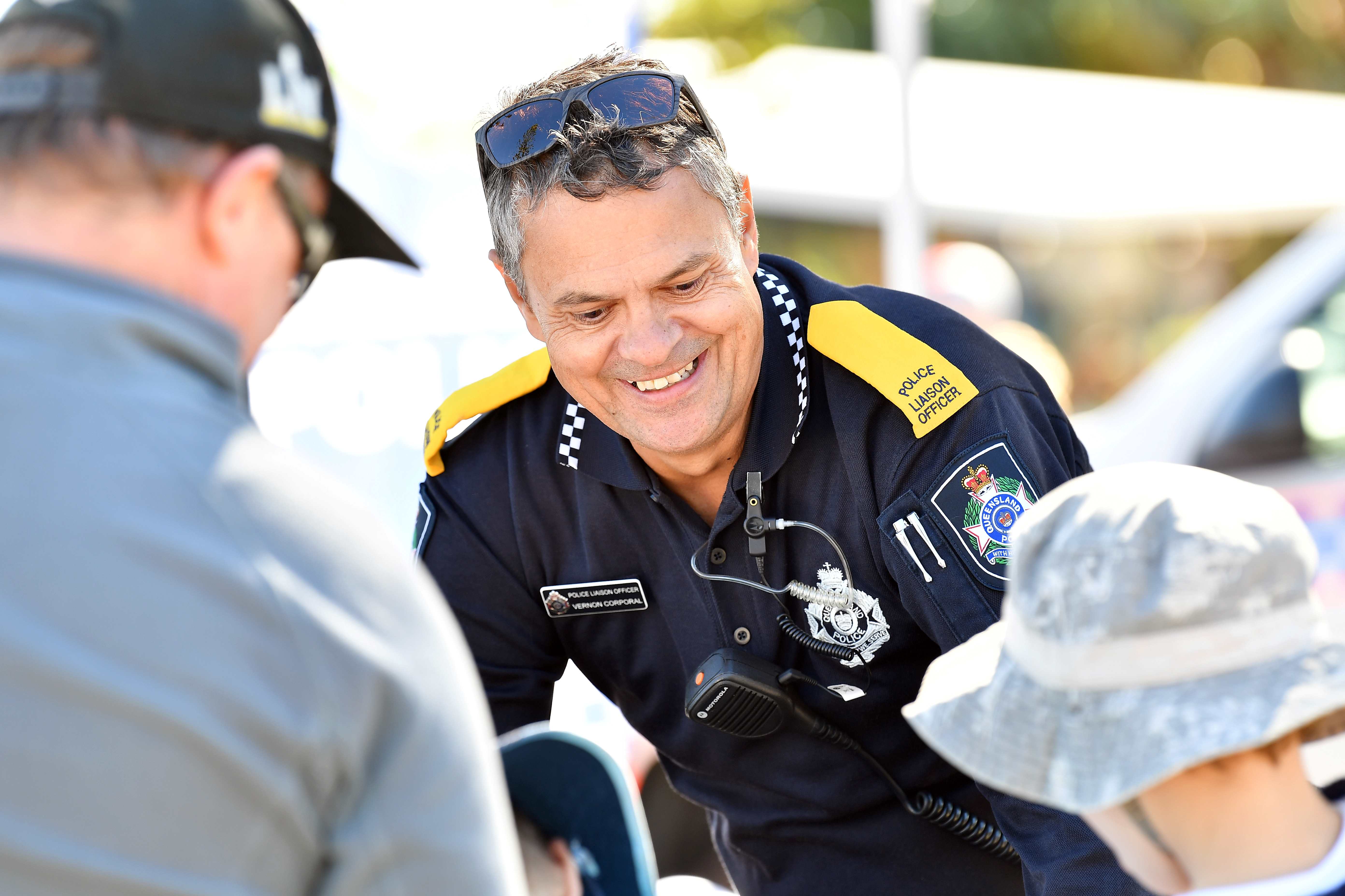 A smiling police officer bends down to talk to some children.