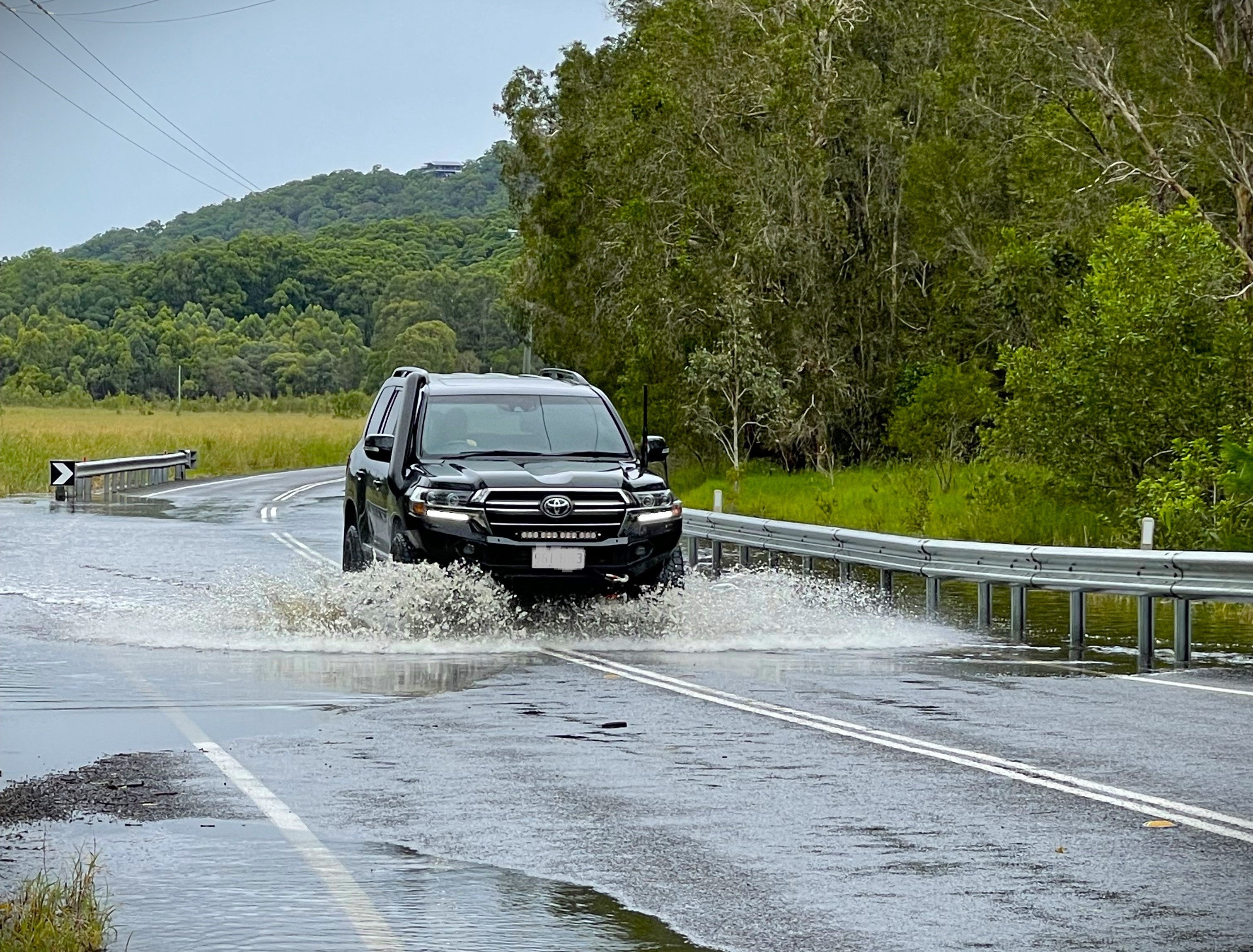 A 4WD is driving through water that is across a country road.