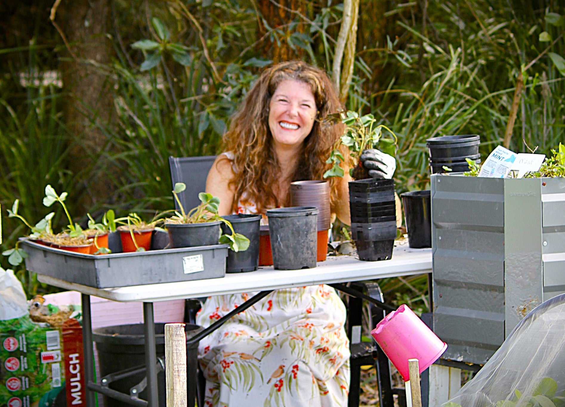 A smiling volunteer sits behind a table potting seedlings.
