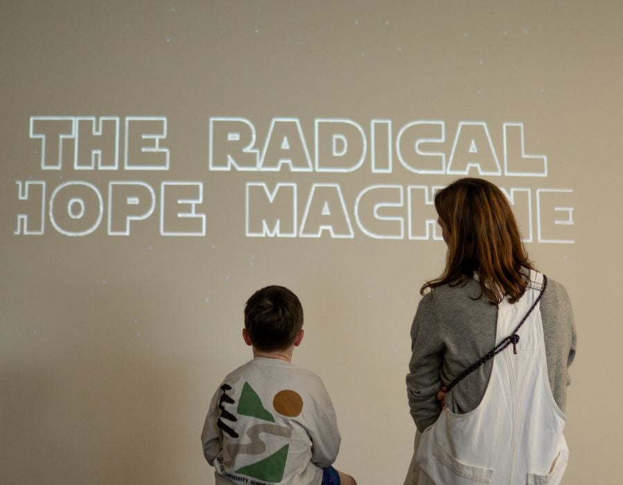 A seated boy and an adult woman look at a projected image that reads “Radical Hope Machine.”