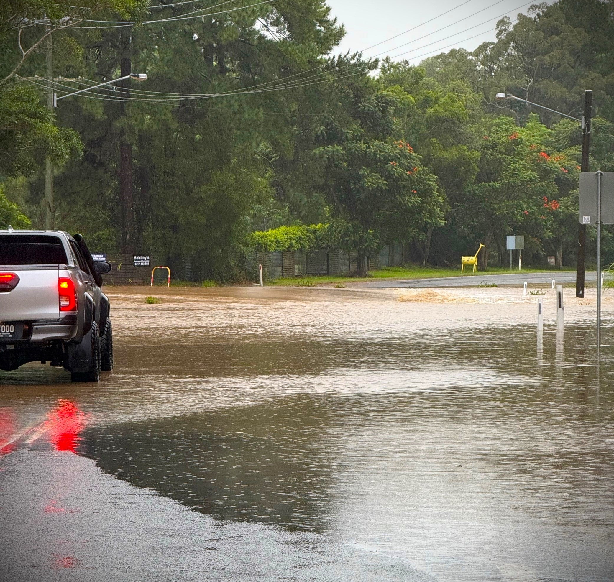 A ute is parked at the edge of flood water at Connection Road in Glenview.