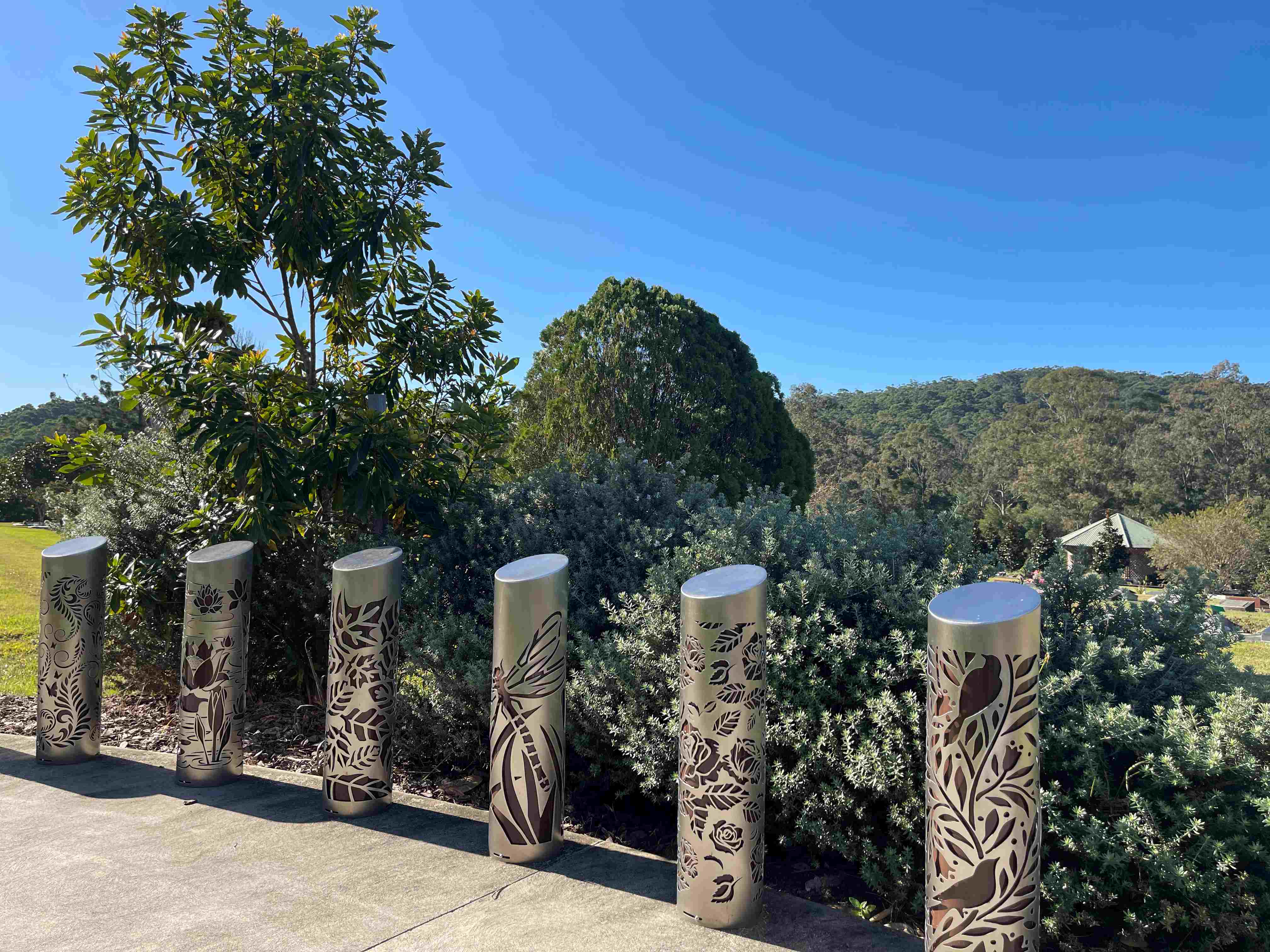 A row of engraved pillars are in the foreground, with green hills in the background, at Kulangoor Cemetery.