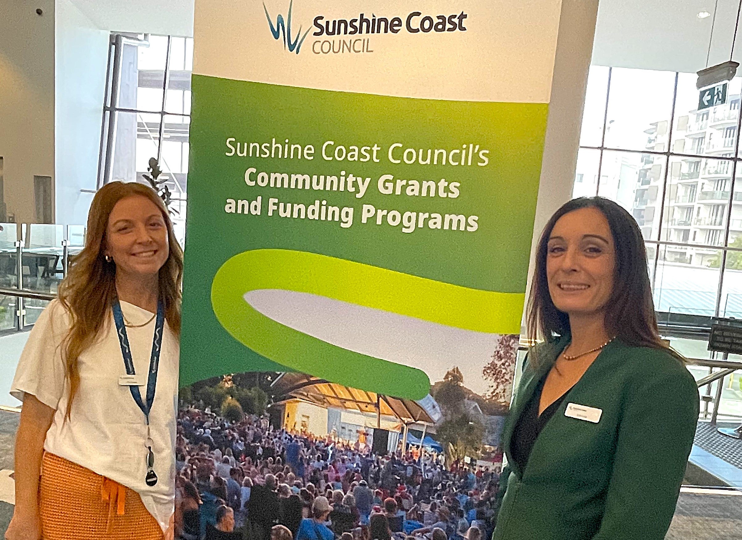 Two smiling women flank a sign that says community grants and funding.