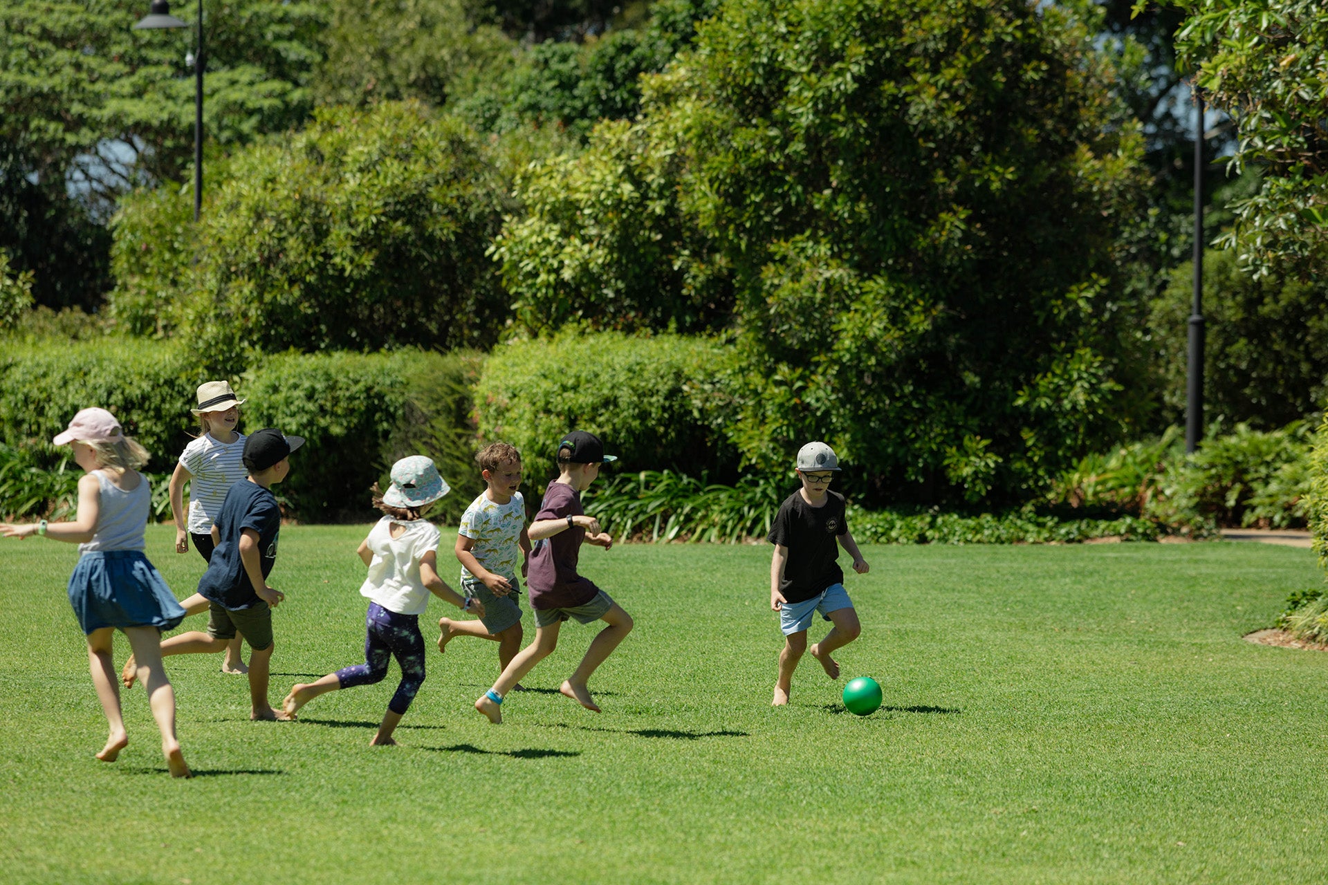 A group of happy children kicking a ball around a green open space on a sunny day in a Council park