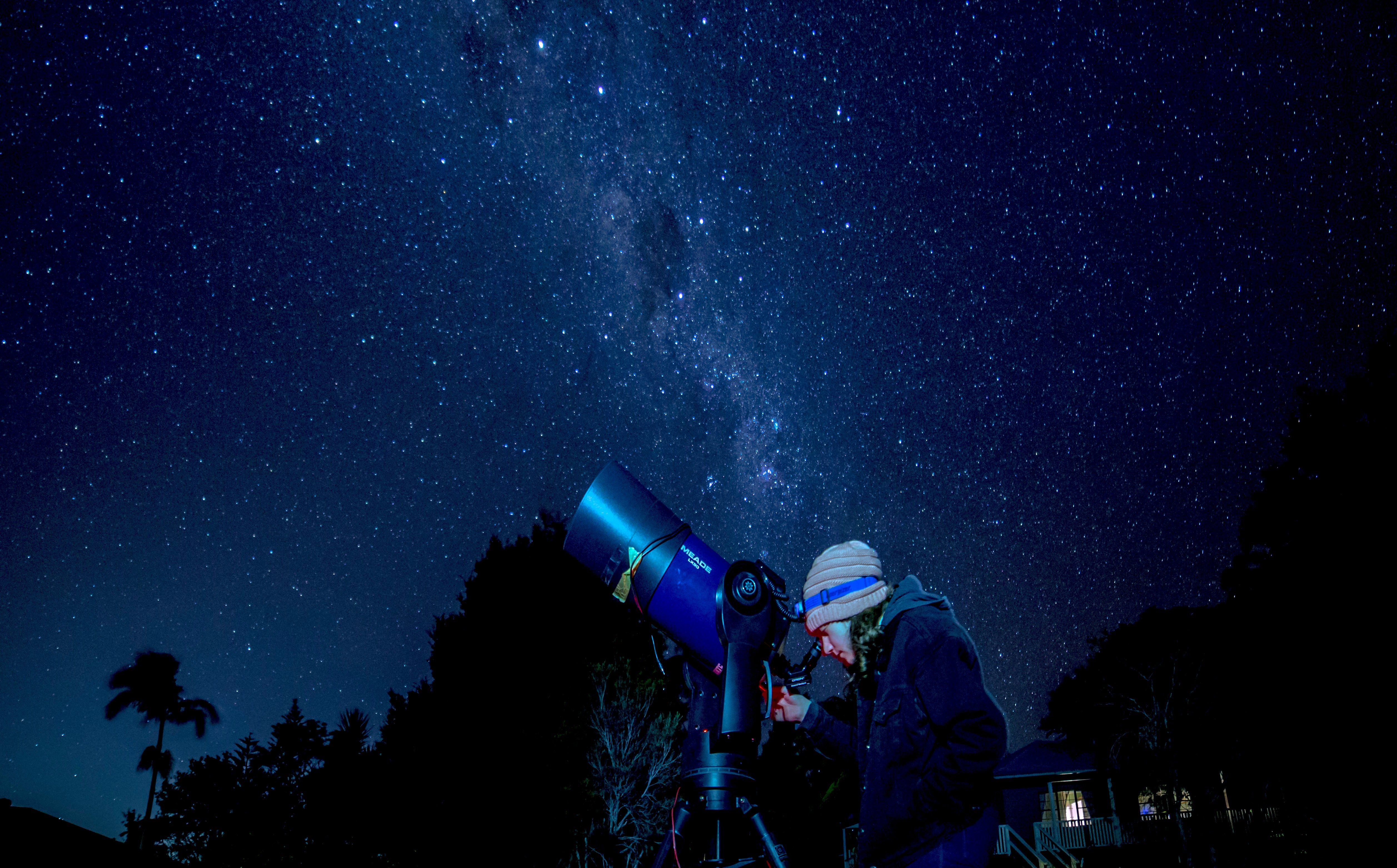 A young person looks at a starry night sky through a telescope.