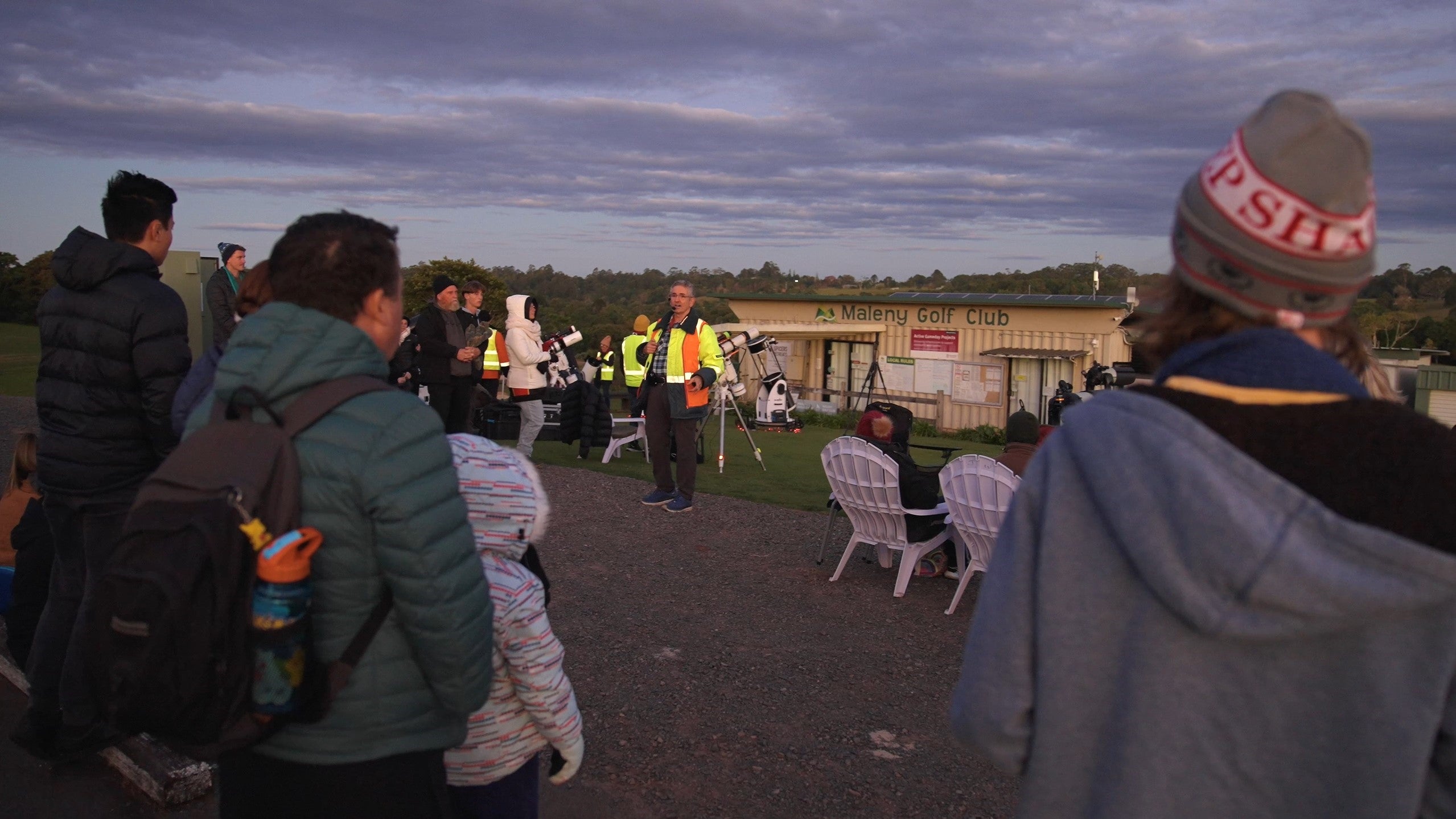 Dr Ken Wishaw speaks to a crowd of people at twilight.