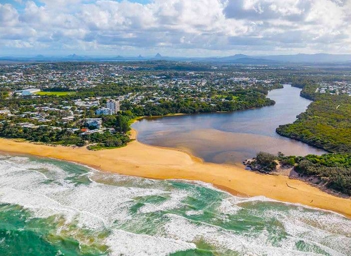 An aerial view of the Sunshine Coast shows a river and the ocean with a strip of sand between the two.